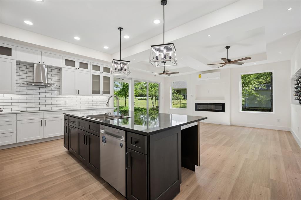 105 Buckboard Trail Oak Point, TX 75068 - Photo 7 of 27 Two tone kitchen with a kitchen island with sink, a glass covered fireplace, light wood finished floors, stainless steel dishwasher, and two tone cabinets. Space for two undercabinet refrigerators.