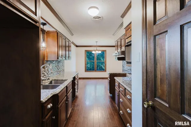 a view of an empty room with wooden floor and a kitchen