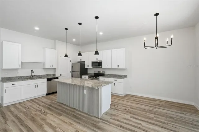 a kitchen with granite countertop a refrigerator a sink a stove and wooden floors