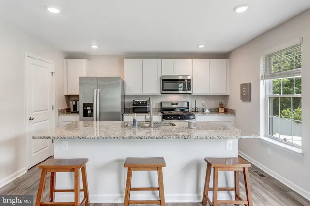 a kitchen with stainless steel appliances granite countertop a sink a stove a refrigerator cabinets and a dining table with wooden floor