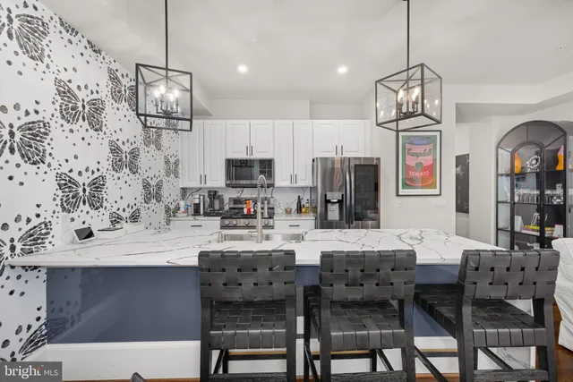 a kitchen with stainless steel appliances kitchen island granite countertop a dining table chairs and a refrigerator