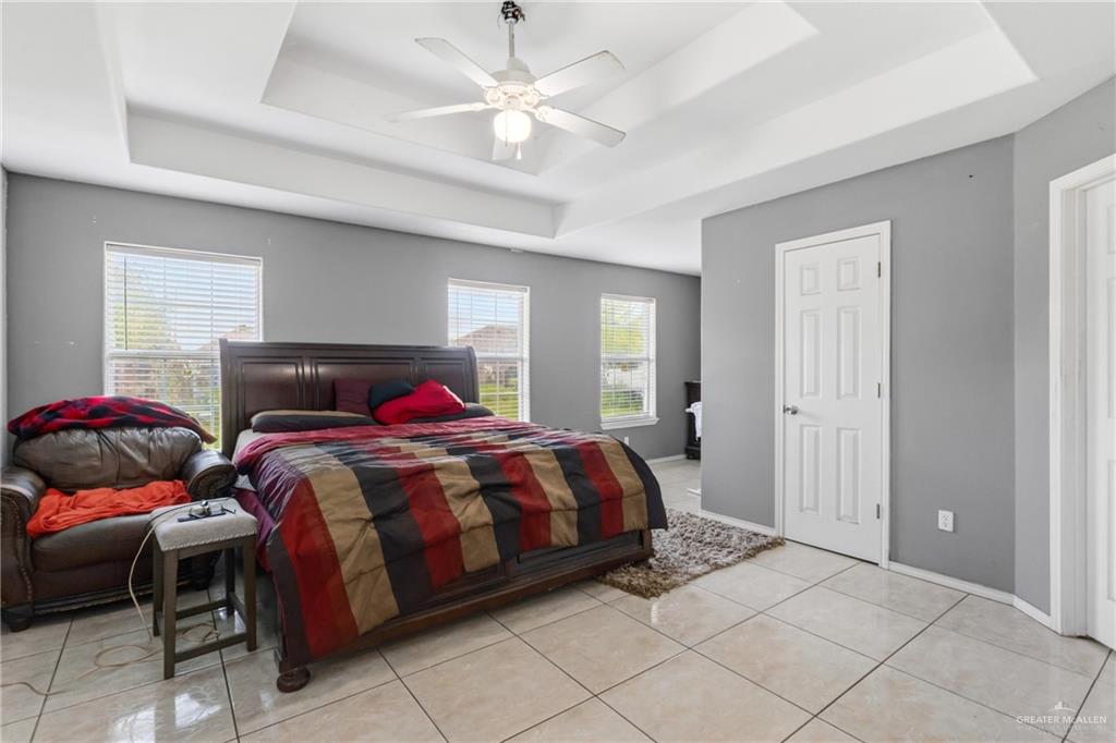 402 Mockingbird Lane Edcouch, TX 78538 - Photo 10 of 25 Spacious room featuring multiple windows, a tray ceiling with a ceiling fan, light-toned tile flooring, and neutral gray walls