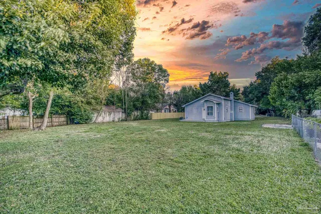 a view of a wooden house with a yard and large tree