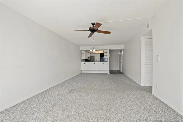an empty room with chandelier fan and windows