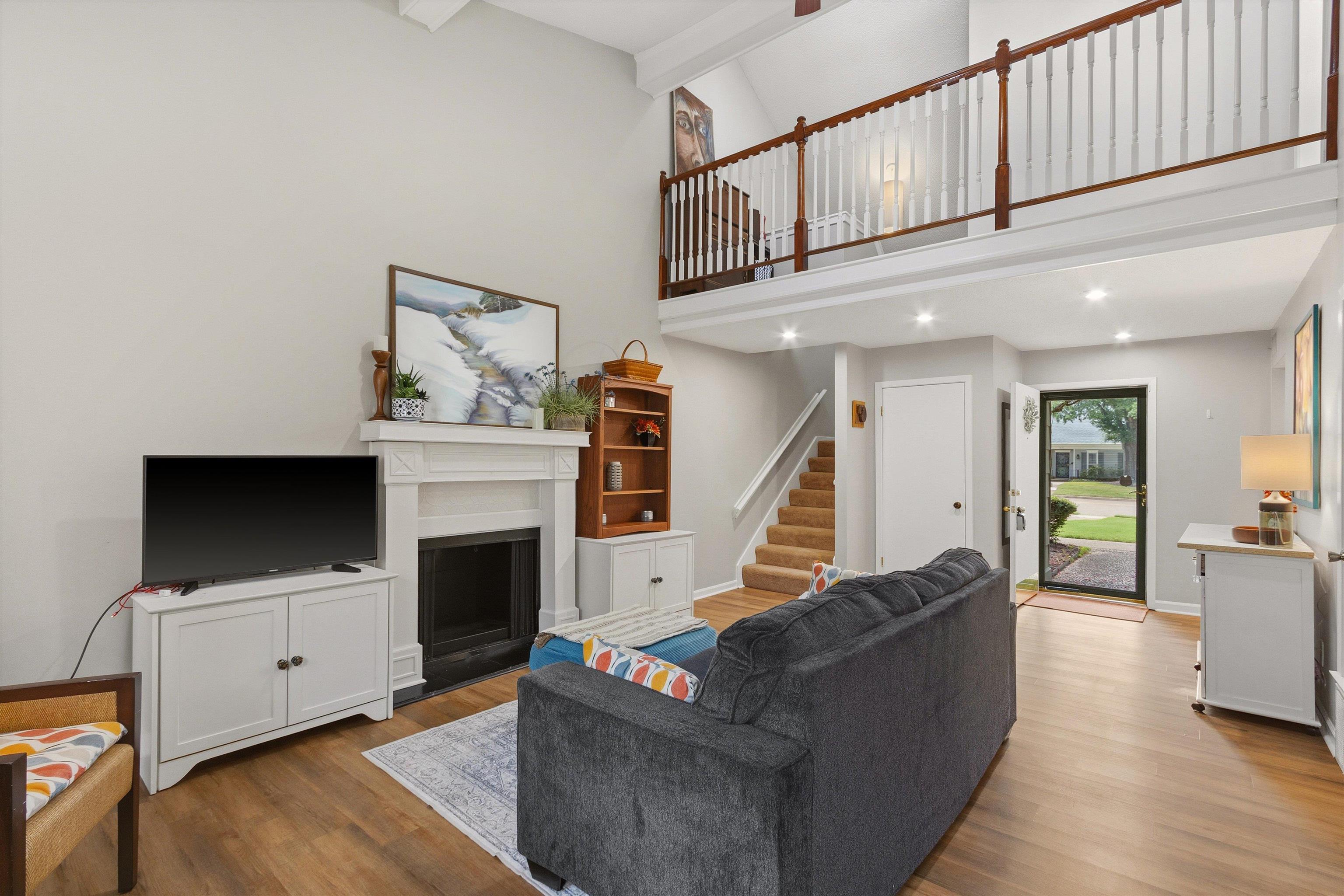 1906 Allenby Road, Unit 16 Germantown, TN 38139 - Photo 11 of 31 Vaulted ceiling with exposed beams, wood-finish flooring, fireplace with a white mantel, staircase with carpeting, and a second-level open railing