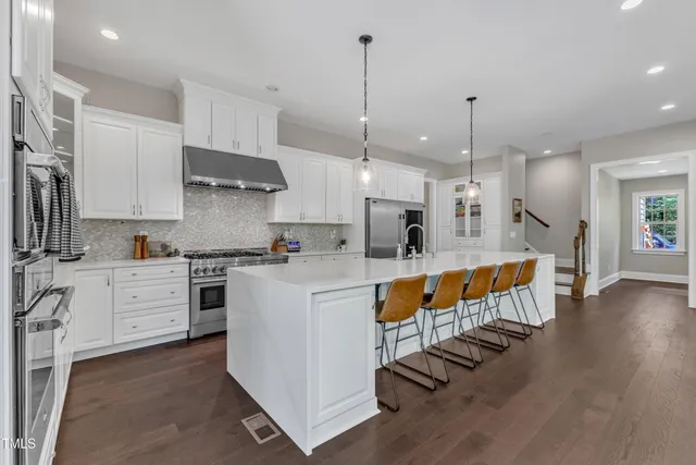 a kitchen with stainless steel appliances kitchen island granite countertop a dining table chairs and white cabinets