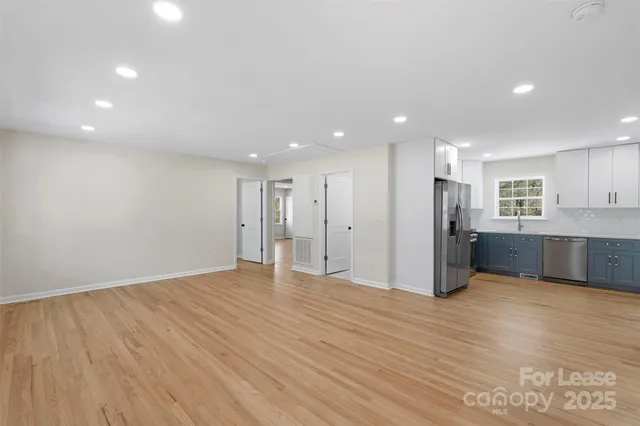 a view of an empty room with wooden floor and a kitchen