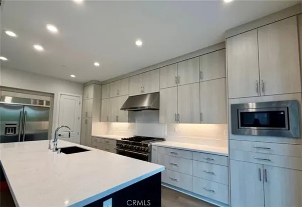 a kitchen with stainless steel appliances a stove a sink a microwave a refrigerator a cabinets and wooden floor