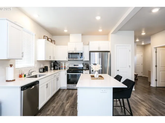 a open kitchen with stainless steel appliances kitchen island granite countertop a stove a sink a refrigerator white cabinets and wooden floor