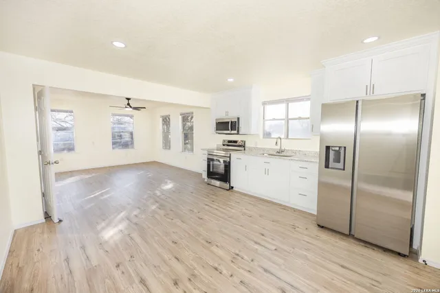 a kitchen with granite countertop a refrigerator oven a sink dishwasher and white cabinets with wooden floor