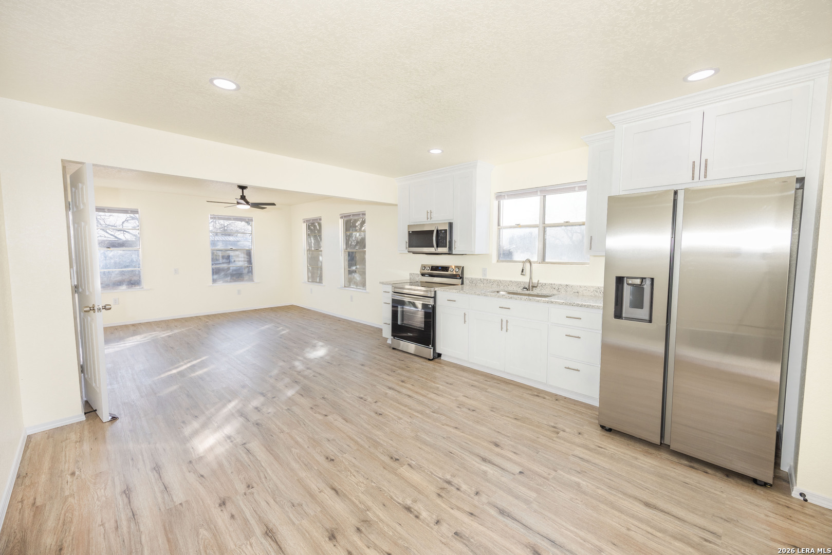 523 A Rossville Road Devine, TX 78016 - Photo 5 of 31 a kitchen with granite countertop a refrigerator oven a sink dishwasher and white cabinets with wooden floor
