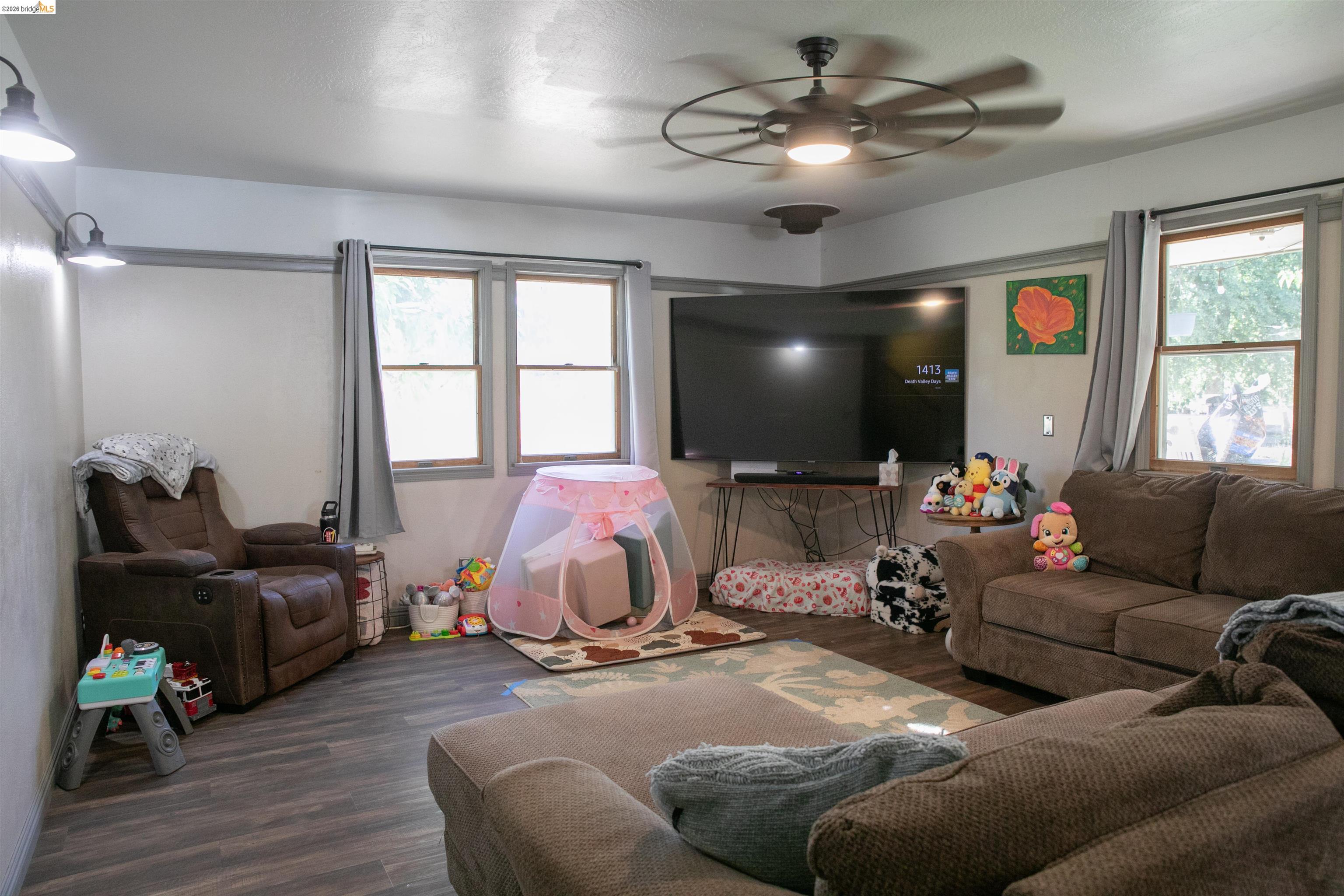 20982 Shaws Flat Road Sonora, CA 95370 - Photo 7 of 26 Living area featuring wood-finish flooring, multiple windows providing natural light, a ceiling fan with integrated lighting, and wall-mounted sconces