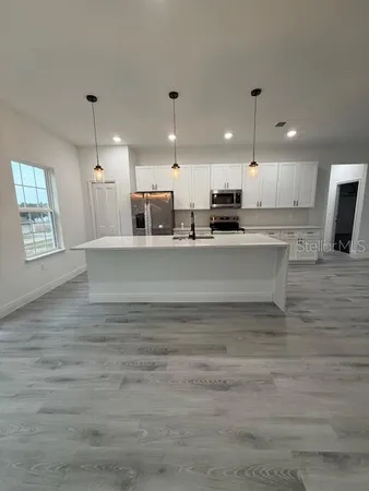 a large kitchen with kitchen island a stove a sink a refrigerator white cabinets and couches with wooden floor