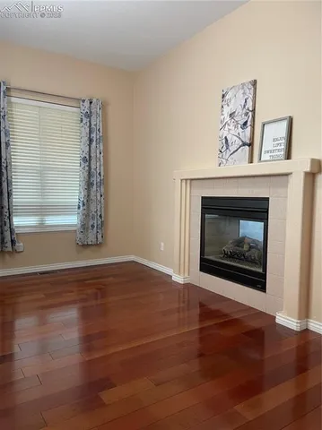 a view of an empty room with wooden floor and a fireplace