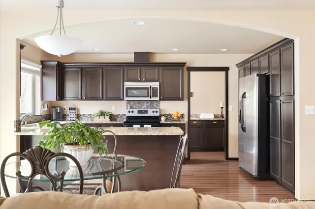 a kitchen with stainless steel appliances granite countertop a refrigerator a stove top oven and a sink with wooden floor