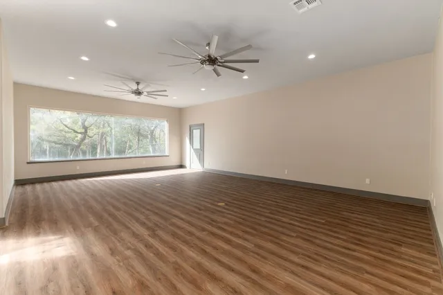 an empty room with wooden floor fan and windows