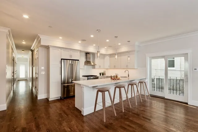 a kitchen with stainless steel appliances a dining table chairs refrigerator and wooden floor