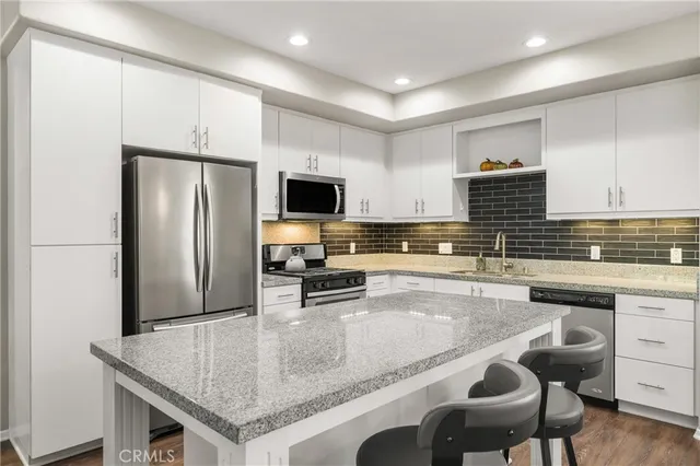 a kitchen with stainless steel appliances kitchen island granite countertop a refrigerator oven a stove a sink a dining table and chairs with wooden floor
