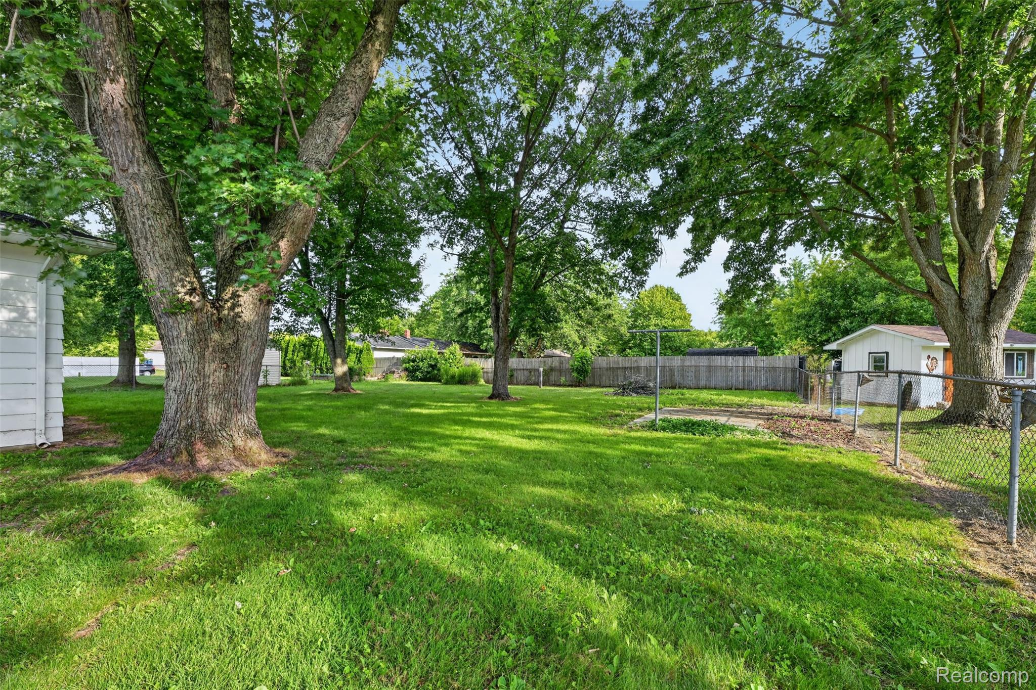 5457 Reid Road Swartz Creek, MI 48473 - Photo 49 of 51 Expansive backyard featuring a manicured lawn, established shade trees, wood privacy fencing, and a chain-link fence section