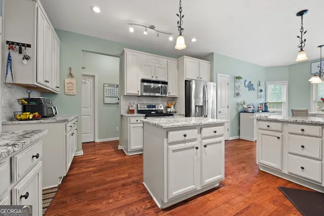 a large kitchen with stainless steel appliances kitchen island granite countertop a refrigerator a stove a sink dishwasher and white cabinets with wooden floor
