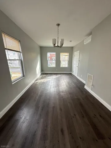 an empty room with wooden floor chandelier and windows