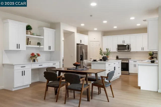 a kitchen with stainless steel appliances kitchen island granite countertop a dining table chairs and a refrigerator