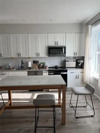 a kitchen with stainless steel appliances granite countertop a stove top oven a refrigerator a sink and white cabinets with wooden floor