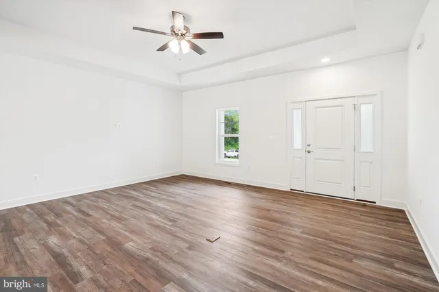 an empty room with wooden floor ceiling fan and windows