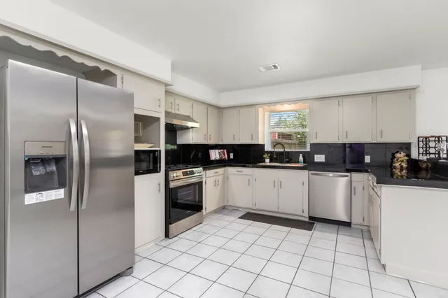 a kitchen with granite countertop white cabinets sink and stainless steel appliances