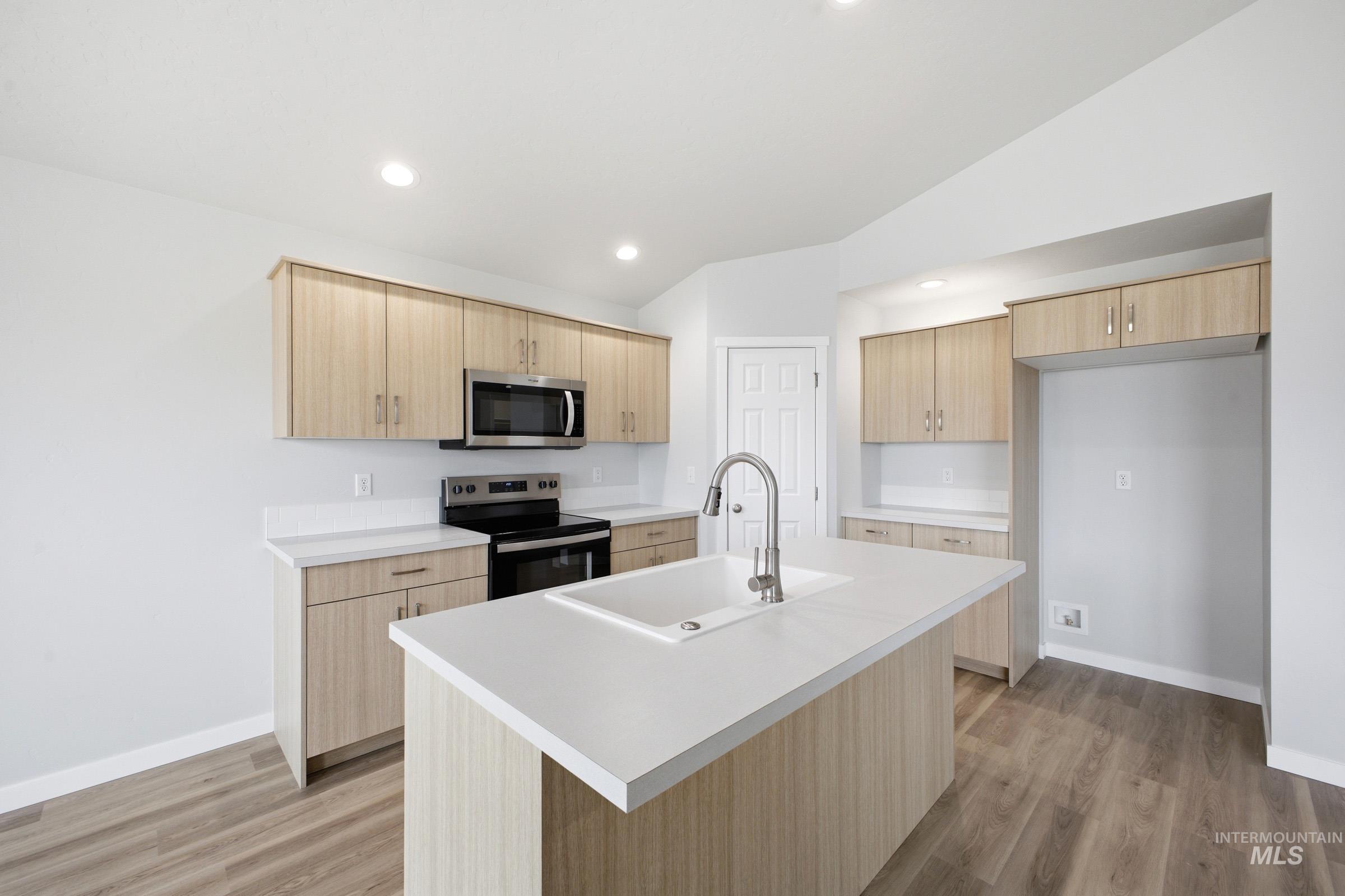 1598 Sunday River Street Middleton, ID 83644 - Photo 4 of 17 Open-concept kitchen featuring an oversized island with an integrated sink, light-toned wood-finish cabinetry, solid surface countertops, stainless steel appliances, and recessed lighting