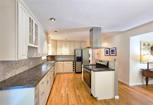 a kitchen with stainless steel appliances granite countertop a stove top oven a sink a refrigerator and white cabinets with wooden floor