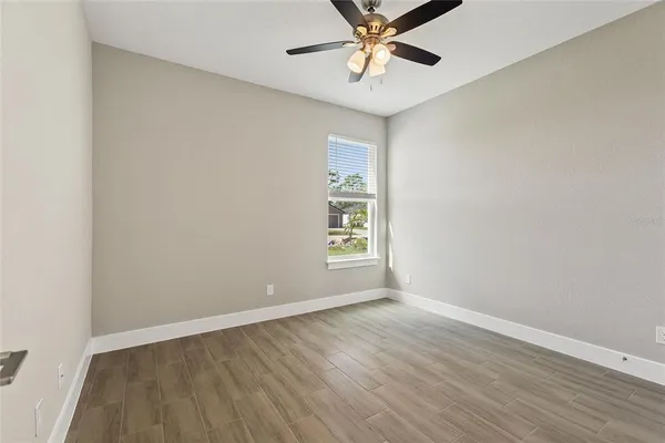 an empty room with wooden floor fan and windows