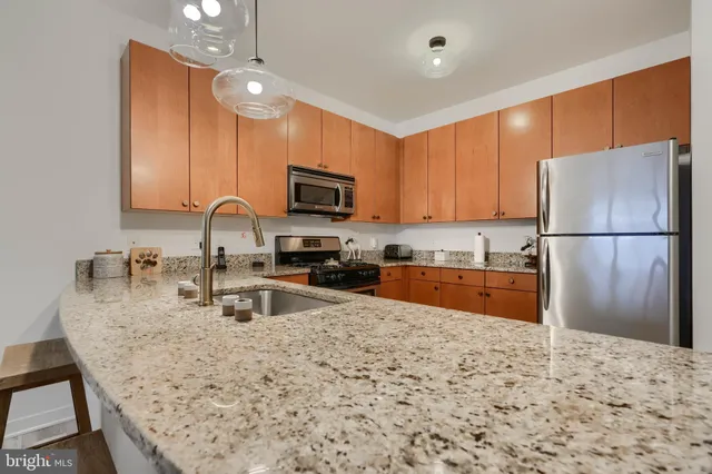 a kitchen with granite countertop a refrigerator a stove a sink a center island a rug and wooden cabinets