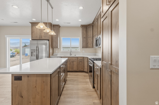 157 West 100 South Joseph, UT 84739 - Photo 10 of 30 Kitchen featuring a kitchen island, wood finish cabinets, stainless steel appliances, decorative light fixtures, and light wood-style floors