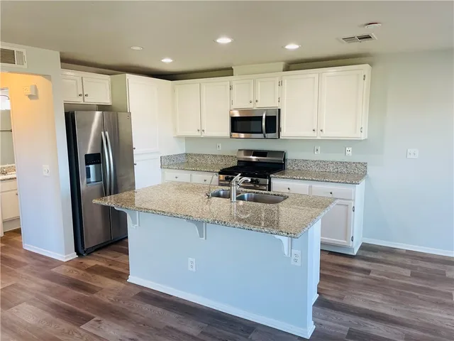 a kitchen with stainless steel appliances granite countertop a refrigerator a stove top oven a sink and dishwasher with wooden floor