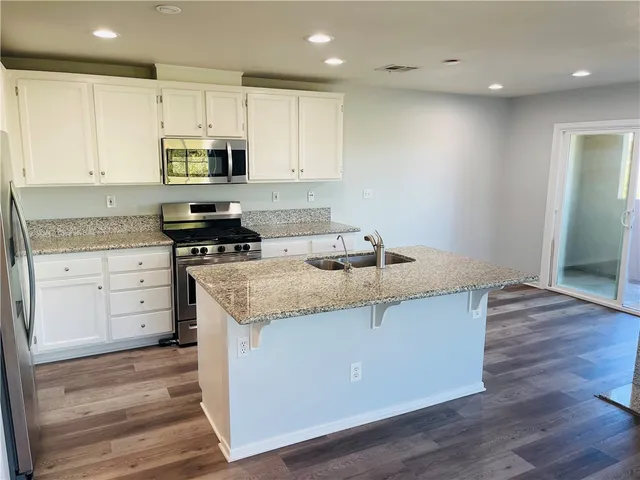 a kitchen with stainless steel appliances granite countertop a sink a stove and a wooden floors