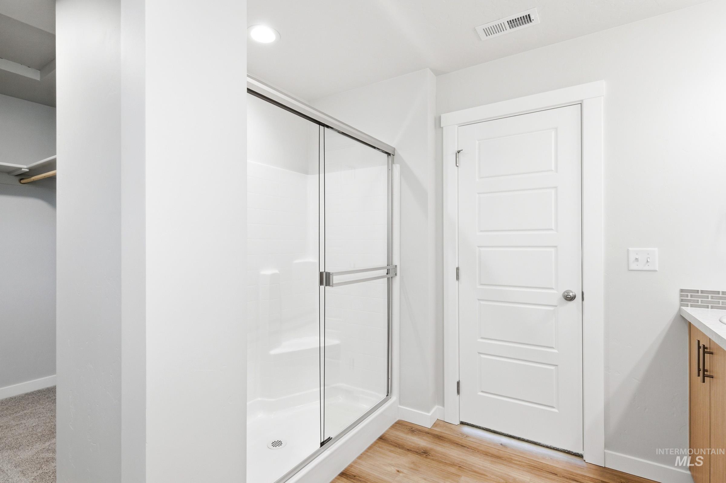 12817 Decatur Street Nampa, ID 83651 - Photo 19 of 19 Modern bathroom featuring a glass-enclosed shower with integrated shelving, wood-finish flooring, a white paneled door, and recessed lighting