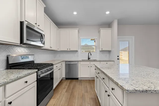 a kitchen with stainless steel appliances granite countertop white cabinets granite counter tops and a hard wood floors