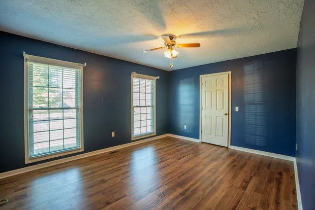 an empty room with wooden floor chandelier fan and windows