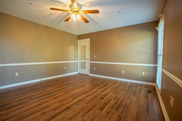 a view of an empty room with wooden floor and a chandelier fan
