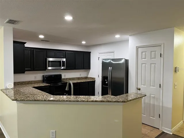 a kitchen with stainless steel appliances granite countertop a refrigerator a stove a microwave oven and a sink