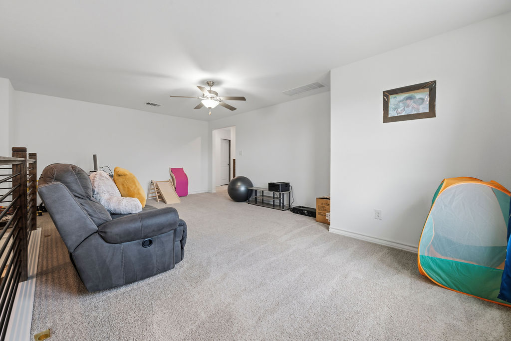 205 Stinchcomb Road Hutto, TX 78634 - Photo 21 of 29 A spacious recreation room offers ample space for various activities, featuring a ceiling fan and soft carpeting.