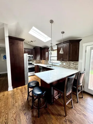 a kitchen with stainless steel appliances kitchen island granite countertop a refrigerator a stove a sink with island chairs and wooden floor