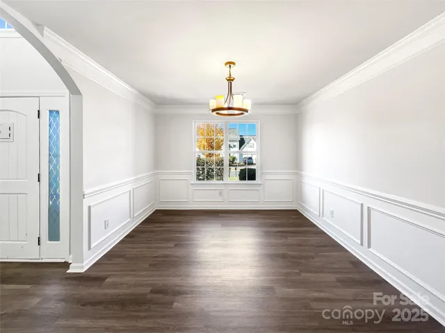 an empty room with wooden floor chandelier and windows