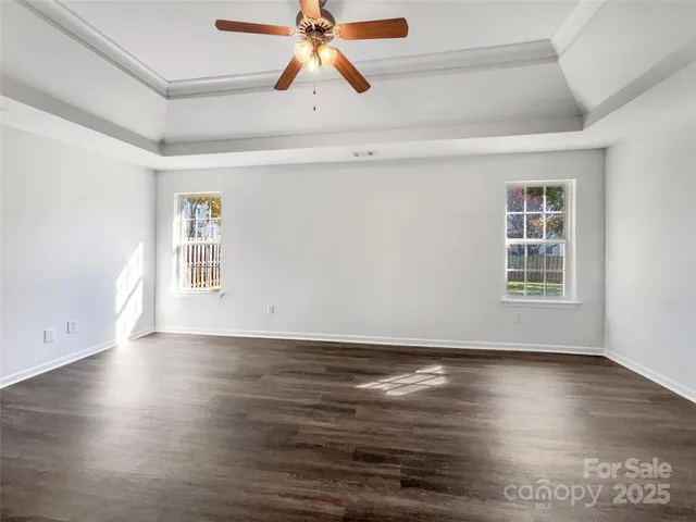 an empty room with wooden floor chandelier fan and windows