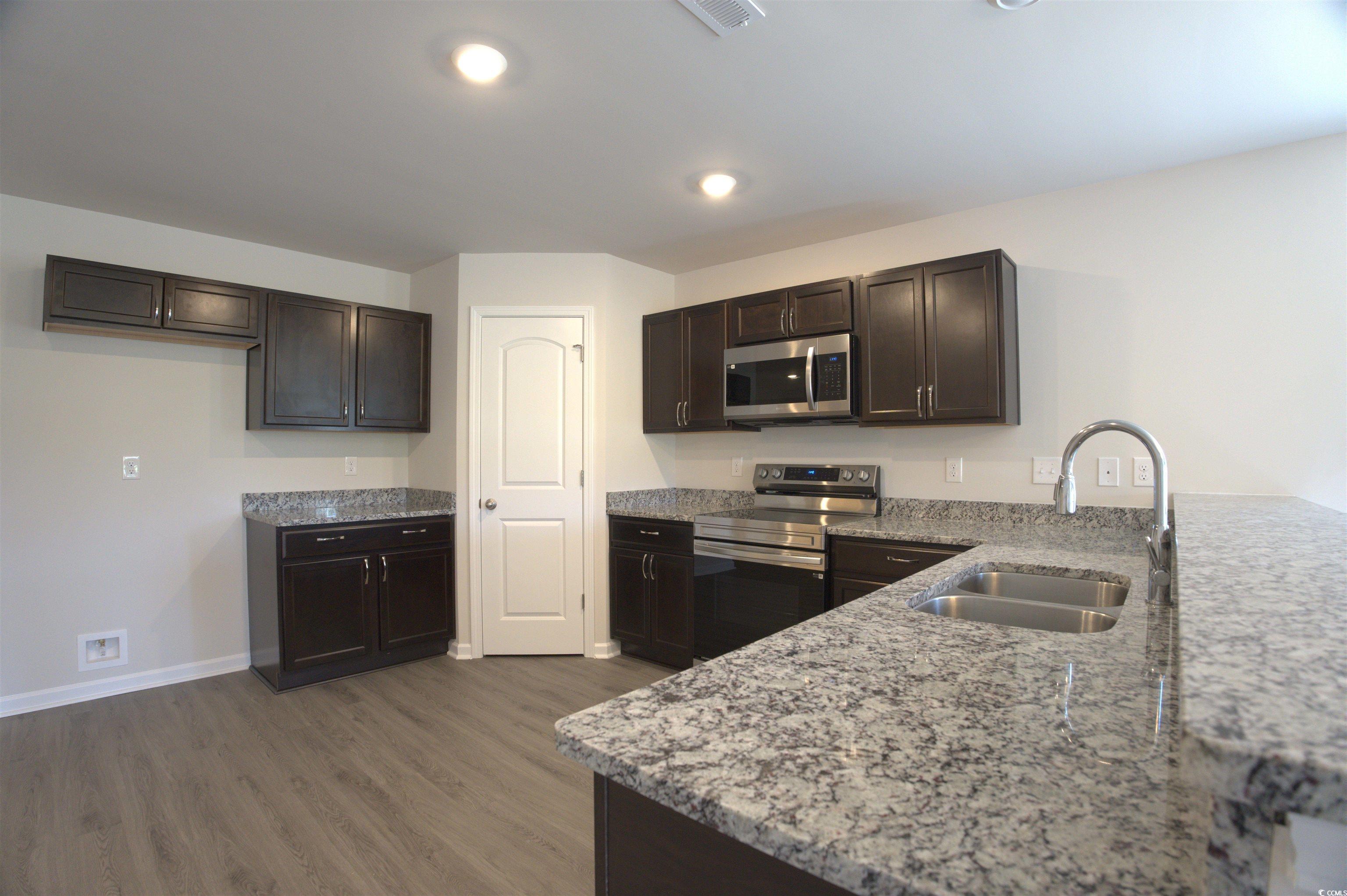 209 Kc Lane Aynor, SC 29511 - Photo 3 of 13 Kitchen with stainless steel appliances, light stone counters, wood finished floors, dark brown cabinetry, and a peninsula