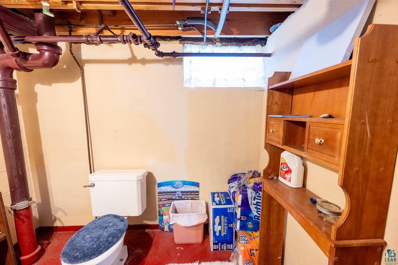 101 2nd Avenue North Biwabik, MN 55708 - Photo 32 of 44 Unfinished basement space featuring exposed ceiling joists and plumbing, a single toilet fixture, and a built-in wood-finish shelving unit