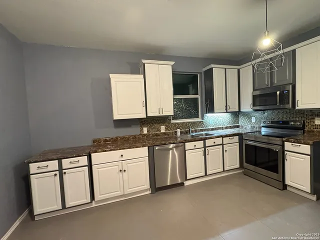 a kitchen with granite countertop white cabinets white stainless steel appliances a sink and a window