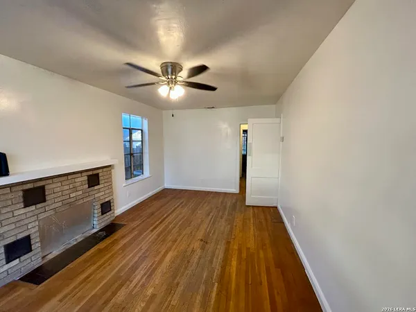 a view of an empty room with chandelier fan and wooden floor