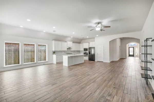 a view of an empty room with wooden floor and a kitchen